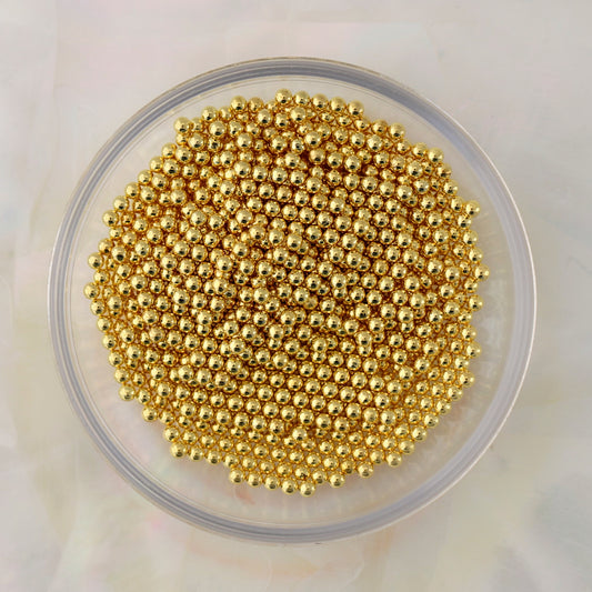 Close-up of small round gold metal caviar beads in three diameters for nail-art decoration.