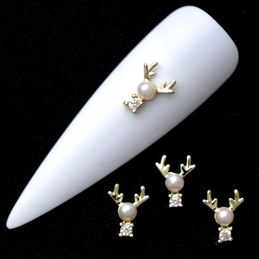 Gold reindeer nail charms with white pearl heads and crystal CZ noses on a white nail tip against a black background