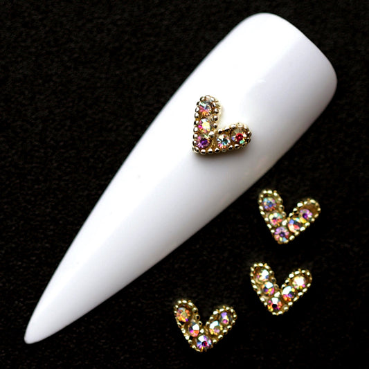 Gold 7×6 mm rope-style heart nail charms paved with iridescent CZ stones displayed on a white nail tip against a black background