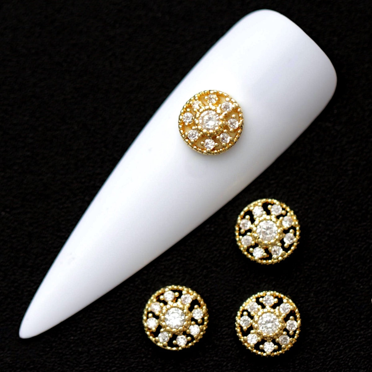 Gold 7 mm round medallion nail charms with central crystal CZ and surrounding mini stones displayed on a white nail tip against a black background