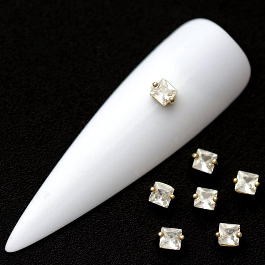 3 mm clear square cubic zirconia nail charms in gold settings displayed on a white nail tip against a black background