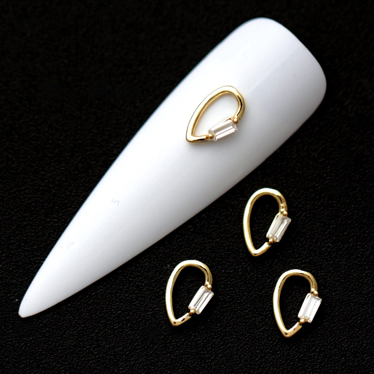 Gold 9×6 mm teardrop loop nail charm with rectangular crystal baguette CZ accent displayed on a white nail tip against a black background