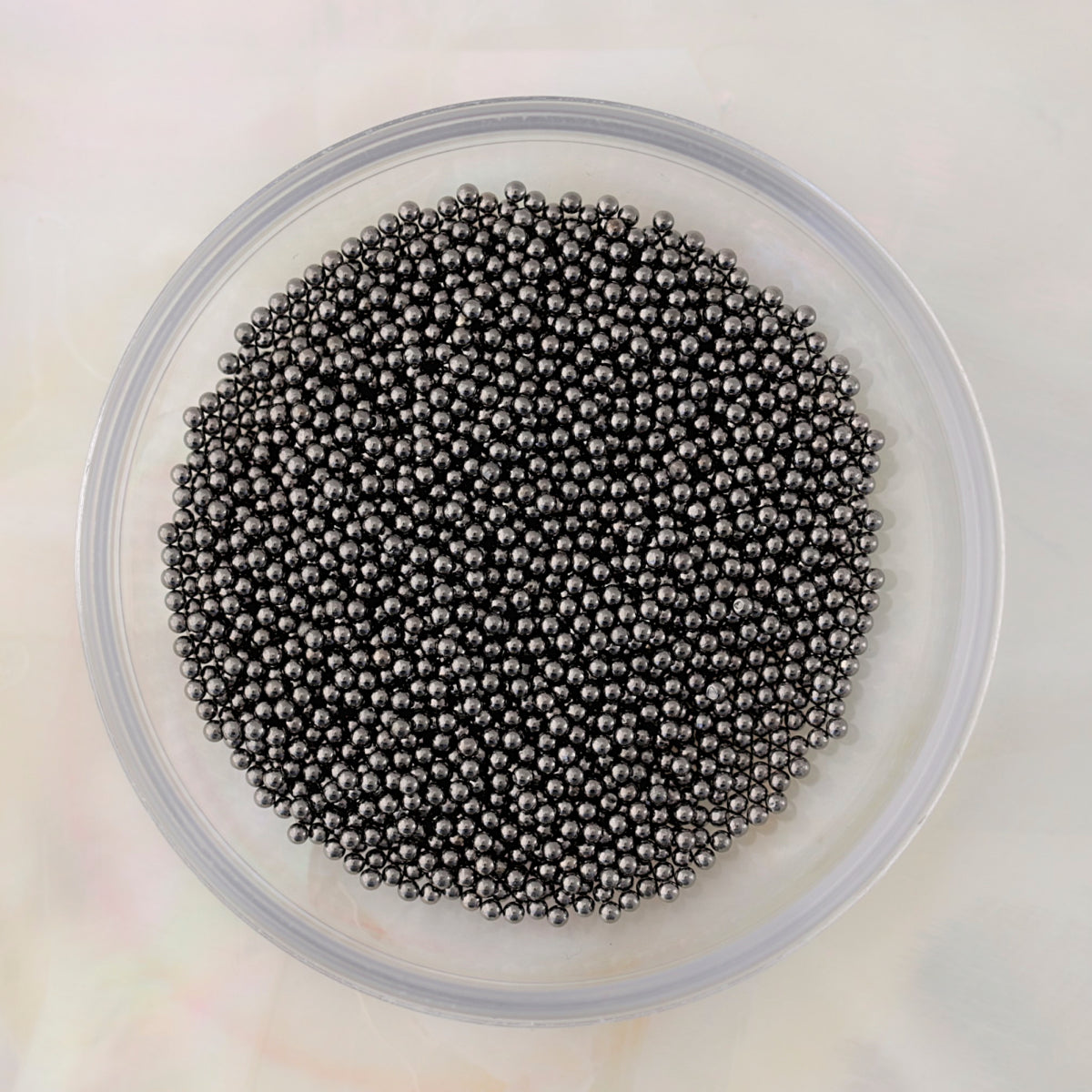 Close-up of small round graphite metal caviar beads in several diameters for nail-art decoration.