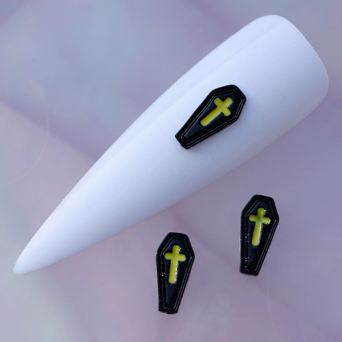 Halloween coffin-shaped nail charm with a glossy black finish, raised border details and a bright neon yellow-green cross in the centre. This gothic nail decoration is ideal for Halloween manicures, horror-inspired designs, spooky accent nails and creative seasonal nail art.