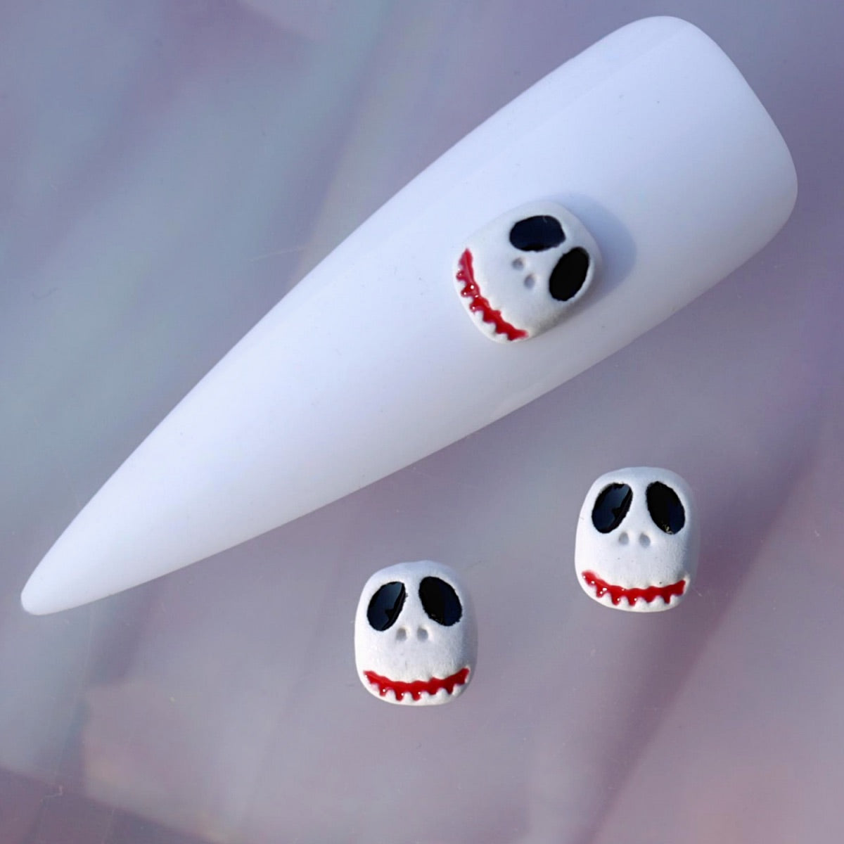 Halloween nail charm featuring the Scruffy Jack skull character. The white skull face has oversized black eyes, small nose details and a distinctive red jagged smile. This playful spooky nail decoration is ideal for Halloween manicures, horror-inspired nail art, seasonal accent nails and creative themed designs.