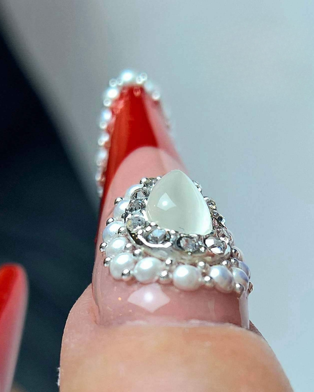 Close-up of a stiletto nail with red tip, pearls and teardrop crystal nail jewelry, demonstrating statement nail accessories from Eunails
