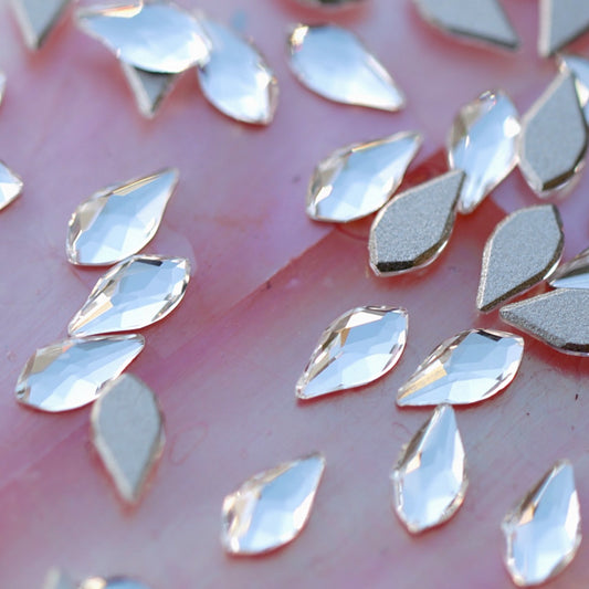 Closeup of clear faceted K9 crystal flatback flame shaped rhinestones showing light refraction and silver metallic base on pink surface