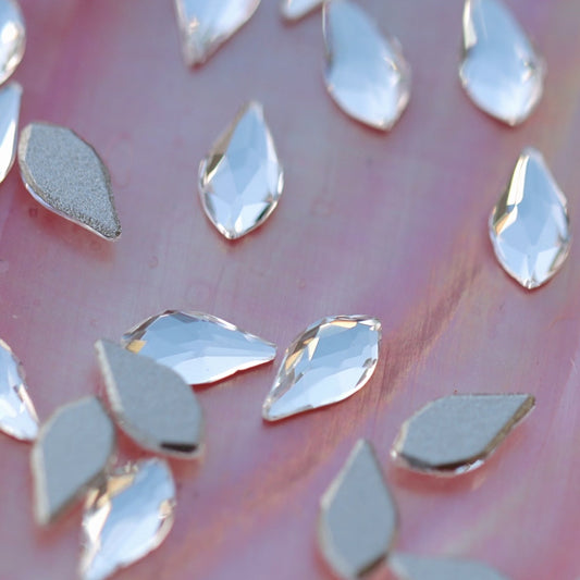 Scattered clear K9 crystal flatback flame rhinestones with silver foil backing on pearlescent pink background for nail art