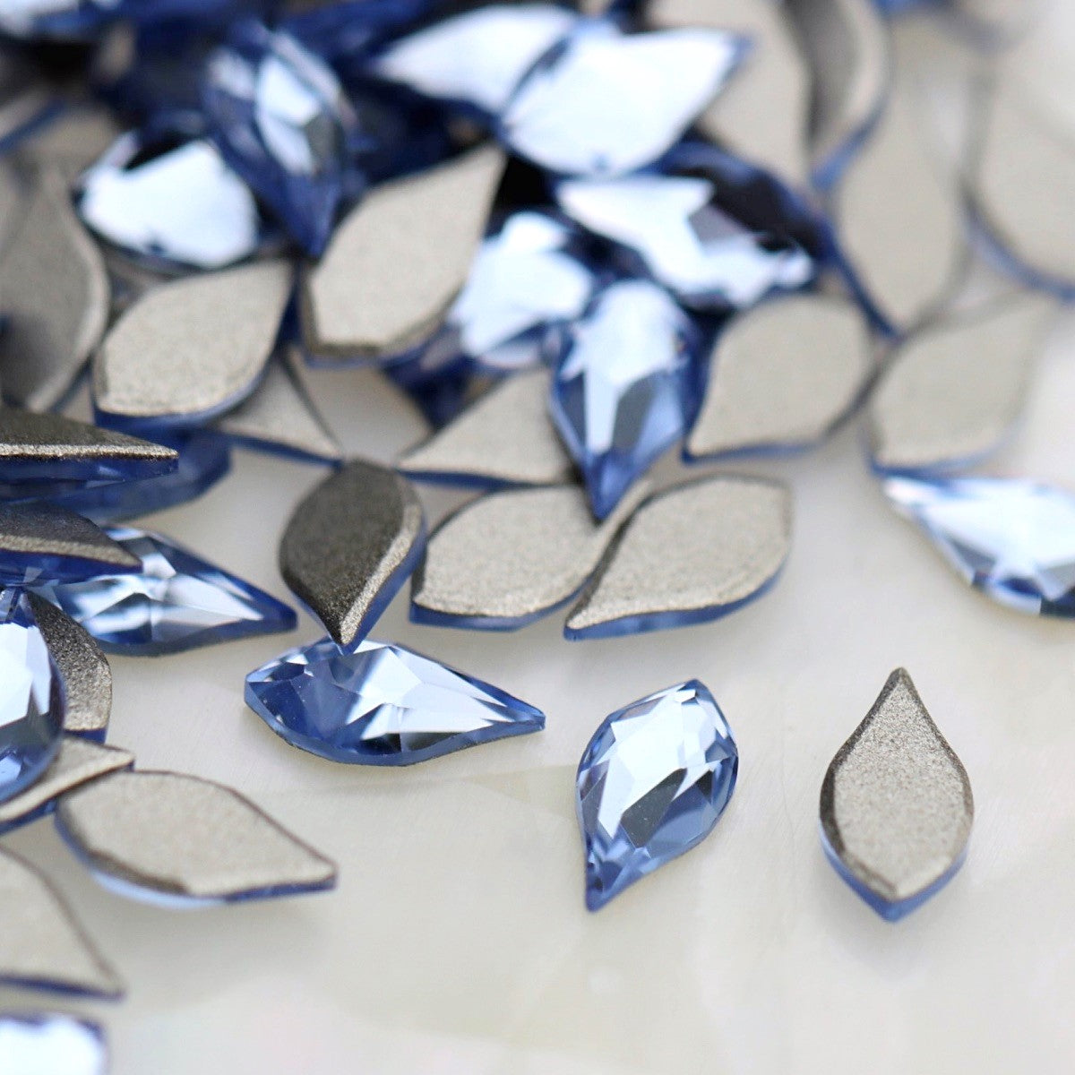 K9 Crystal Flatback Flame Light Sapphire 6×3mm with a pointed light-blue flame shape and faceted reflective surface.