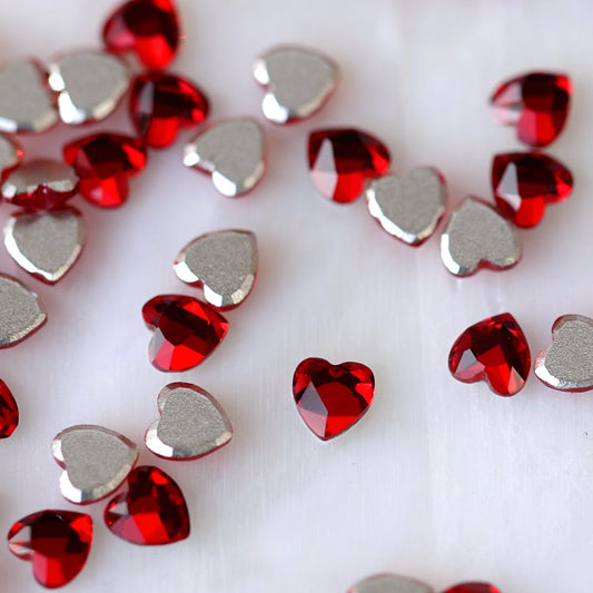 Close-up of faceted 3mm K9 Crystal heart decorations in bright Siam red, showing their reflective surfaces and flat adhesive backs.