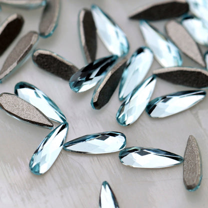 K9 Crystal Flatback Raindrop in Aquamarine Crystal, measuring 6×2mm. The elongated teardrop-shaped crystal has a narrow pointed tip, rounded lower end and faceted front surface. Its transparent light-blue colour reflects pale aqua, icy blue, turquoise, seafoam, soft teal and silvery tones. Ideal for bridal nails, ocean-inspired nail art, mermaid designs, floral manicures, crystal clusters and elegant nail decorations.