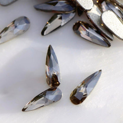 Close-up of slim 6×2mm K9 Crystal raindrops in Black Diamond, showing faceted smoky grey surfaces with silver and graphite reflections.