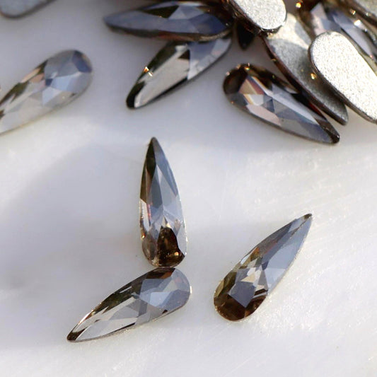 Close-up of slim 6×2mm K9 Crystal raindrops in Black Diamond, showing faceted smoky grey surfaces with silver and graphite reflections.