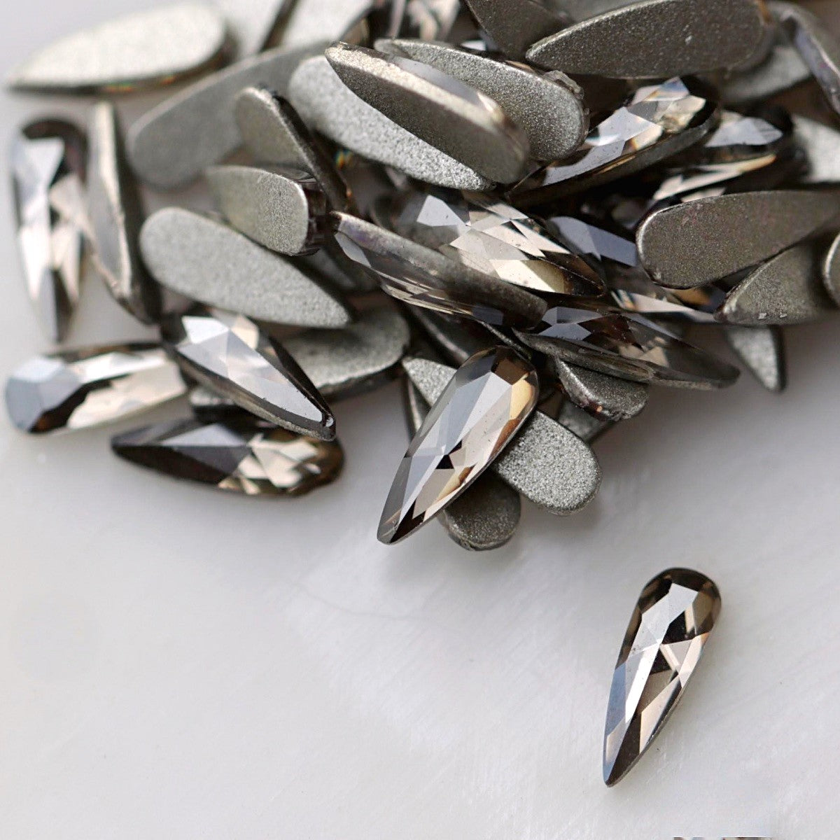 Black Diamond flatback K9 Crystal raindrops displayed from the front and back, highlighting their elongated tapered shape, reflective dark-grey facets and flat adhesive backs.
