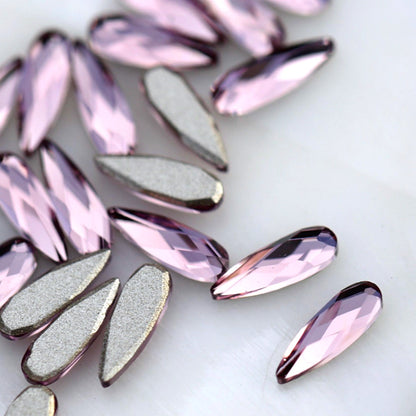 Close-up of slim 6×2mm K9 Crystal raindrops in Light Amethyst, showing faceted pale lavender surfaces with soft lilac and pink reflections.