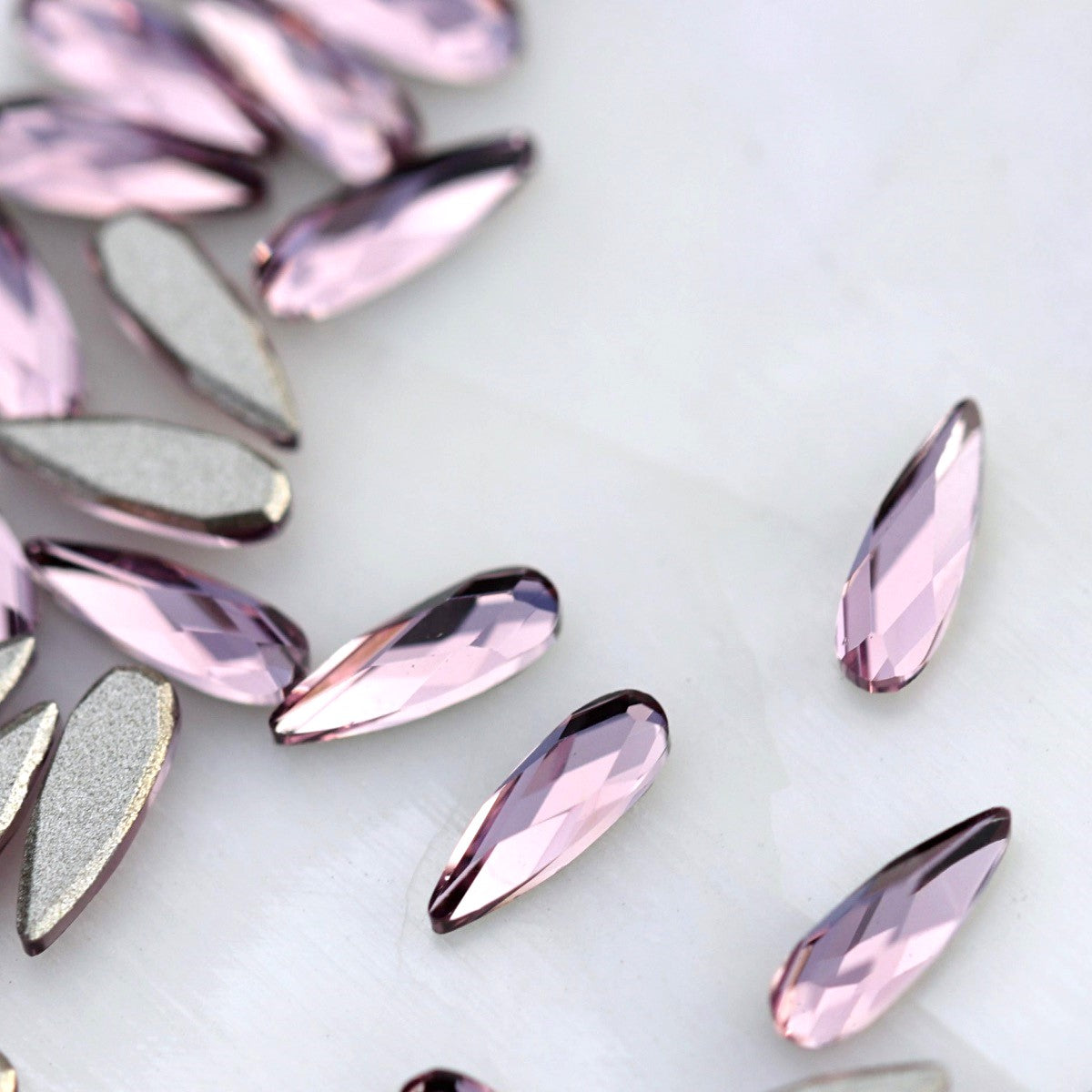 Light Amethyst flatback K9 Crystal raindrops displayed from the front and back, highlighting their elongated tapered shape, soft purple faceted surface and flat adhesive backs.