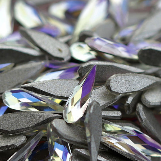 Close-up pile of K9 Crystal flatback raindrop stones in Moonlight color showing translucent facets with lilac and icy blue reflections