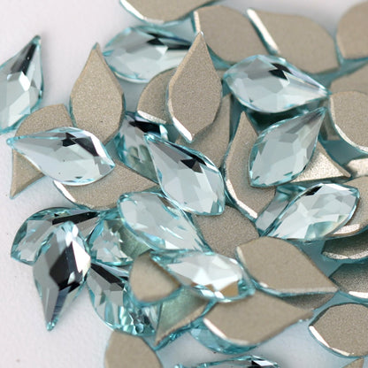 A close-up view of Aquamarine K9 flatback rhombus crystals arranged on a white surface. The diamond-shaped stones feature a refreshing light-blue tone, precision-cut facets, and metallic silver backing that enhances light reflection and creates a bright, multidimensional sparkle. Ideal for nail art, jewelry, fashion accessories, and creative crafts.