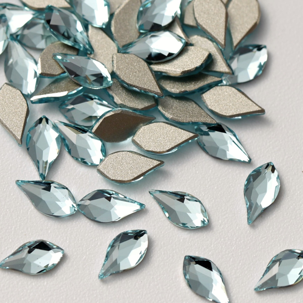 A detailed close-up of Aquamarine K9 crystal rhombus stones displayed on a white background. The elegant diamond-shaped crystals combine a soft blue color with sharp faceting and reflective silver foil backing, making them perfect for geometric nail art, jewelry embellishments, fashion decoration, and DIY creative projects.