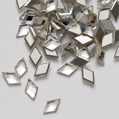 A close-up view of clear Crystal K9 flatback rhombus stones arranged on a white surface. The diamond-shaped crystals feature precision-cut facets and reflective silver foil backings that create bright, multidimensional sparkle. Ideal for geometric nail art, jewelry decoration, fashion accessories, and creative DIY projects.