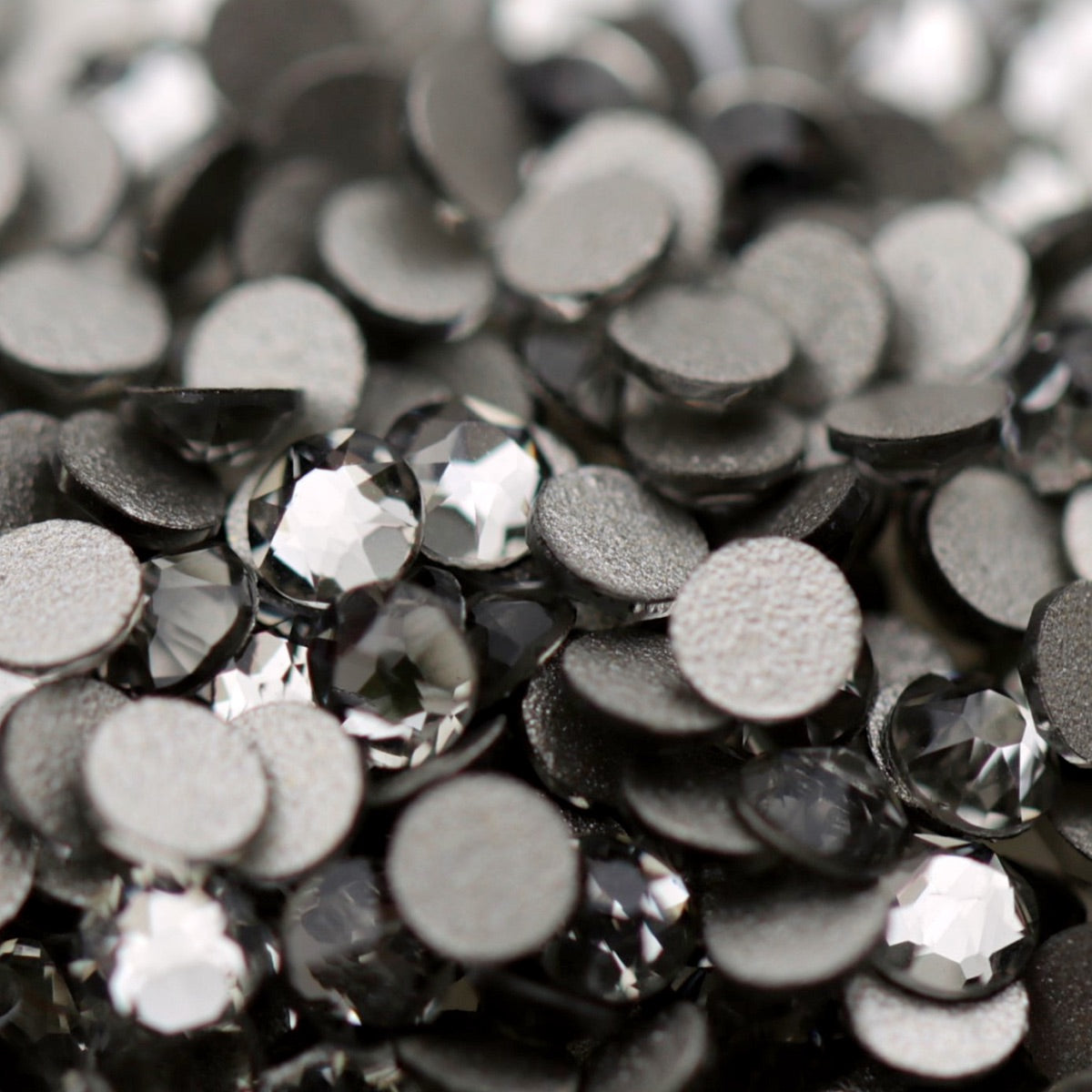 Close-up of round K9 flatback rhinestones in Black Diamond, showing sharp faceting and smoky charcoal, graphite and silver-toned reflections.