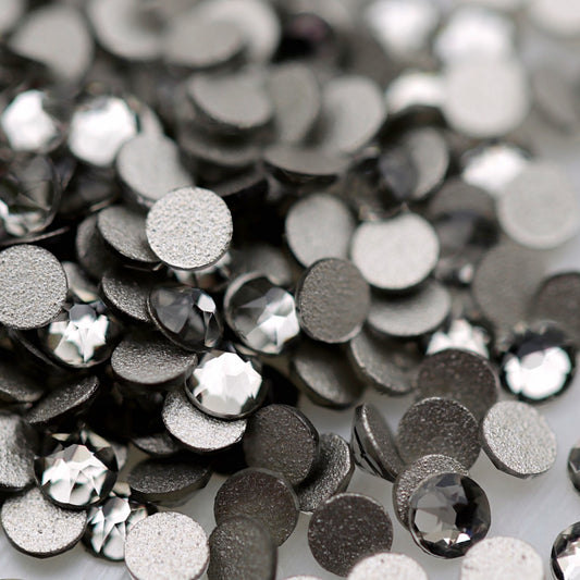 Black Diamond K9 flatback rhinestones displayed from the front and back, highlighting their reflective dark-grey faceted tops and flat backs for nail-art application.