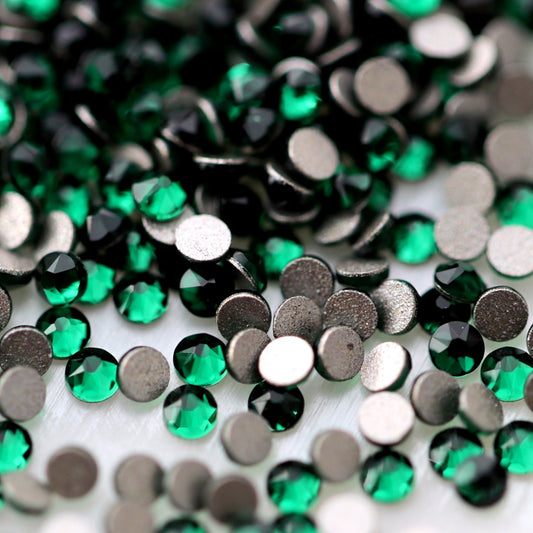 Close-up of round K9 flatback rhinestones in deep Emerald green, showing defined faceting, vivid green reflections and flat backs for nail-art application.