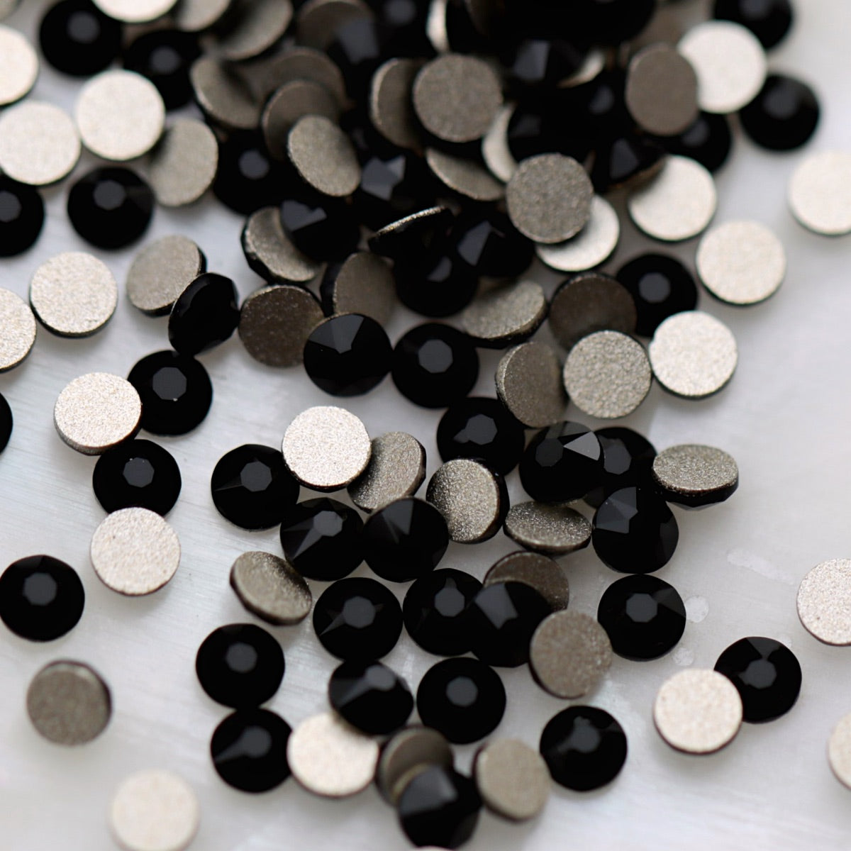 Jet black K9 flatback rhinestones displayed from the front and back, highlighting their glossy dark reflective facets and flat backs for nail-art application.