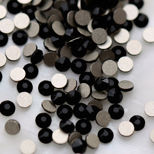 Jet black K9 flatback rhinestones displayed from the front and back, highlighting their glossy dark reflective facets and flat backs for nail-art application.