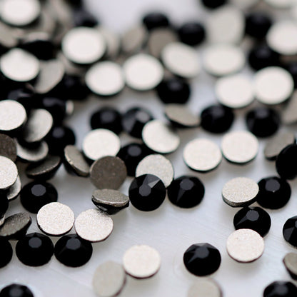 Small faceted Jet black K9 rhinestones scattered on a light background, showing their solid black colour and high-contrast sparkle for gothic and monochrome nail art.
