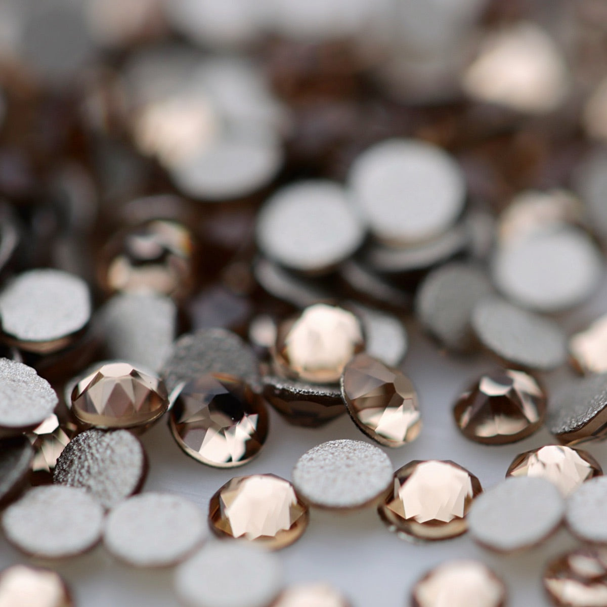 Close-up of round K9 flatback rhinestones in Light Colorado Topaz, showing sharp faceting and transparent pale topaz, champagne and warm golden reflections.