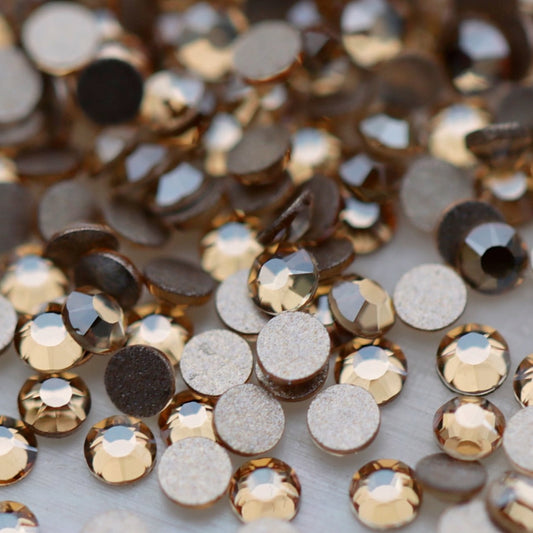 Close-up of round K9 flatback rhinestones in soft Light Peach, showing sharp faceting and warm champagne, beige and pale golden reflections.