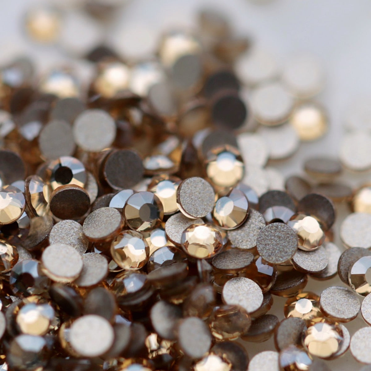 Light Peach K9 flatback rhinestones displayed from the front and back, highlighting their reflective faceted tops and flat backs for nail-art application.