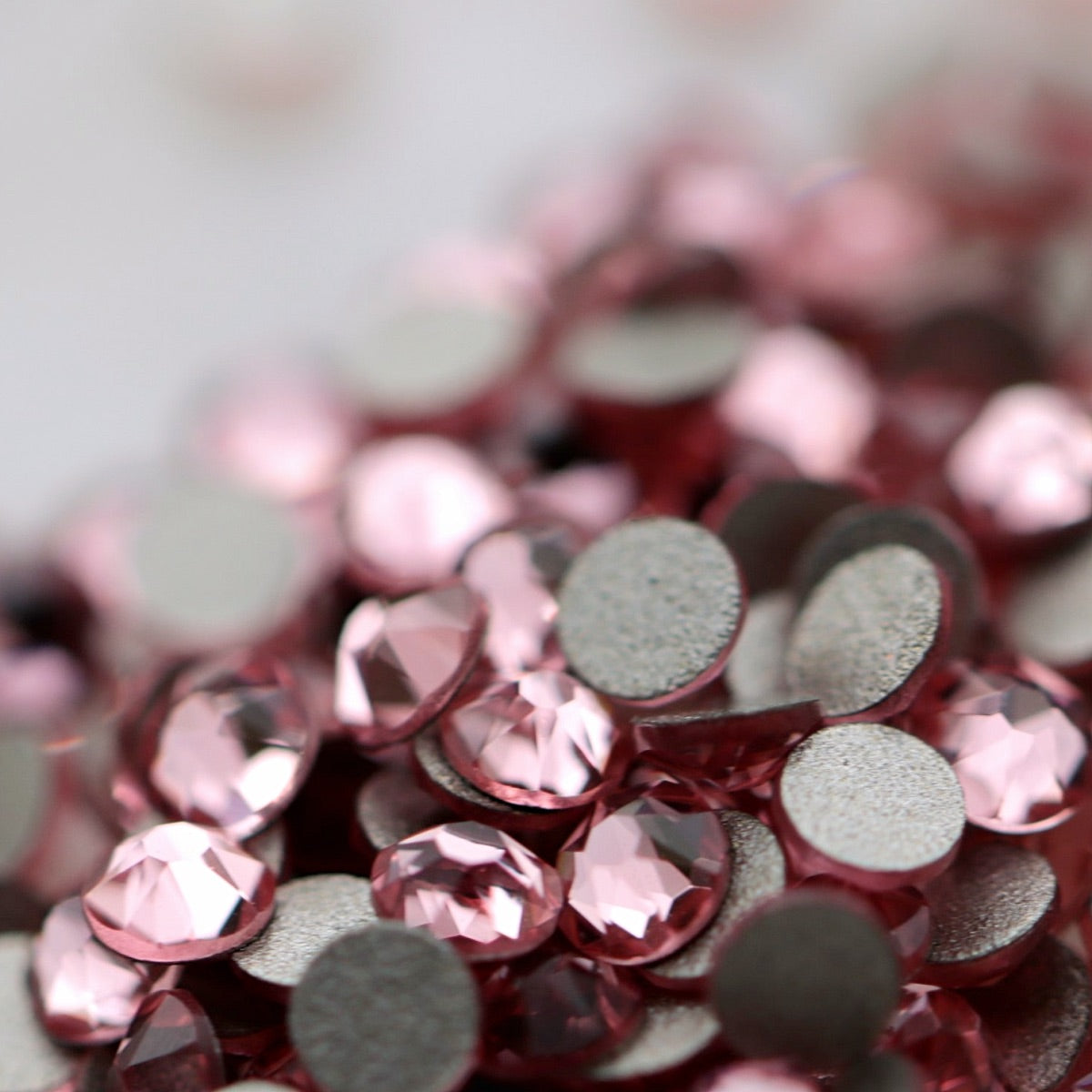 Close-up of round K9 flatback rhinestones in pale Light Rose pink, showing sharp faceting and soft blush-pink reflections.