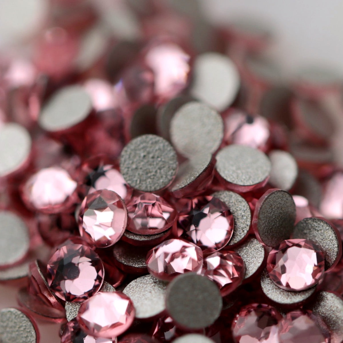 Light Rose pink K9 flatback rhinestones displayed from the front and back, highlighting their reflective faceted tops and flat backs for nail-art application.