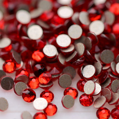 Close-up of round K9 flatback rhinestones in bright Light Siam red, showing sharp faceting and vivid scarlet and cherry-red reflections.