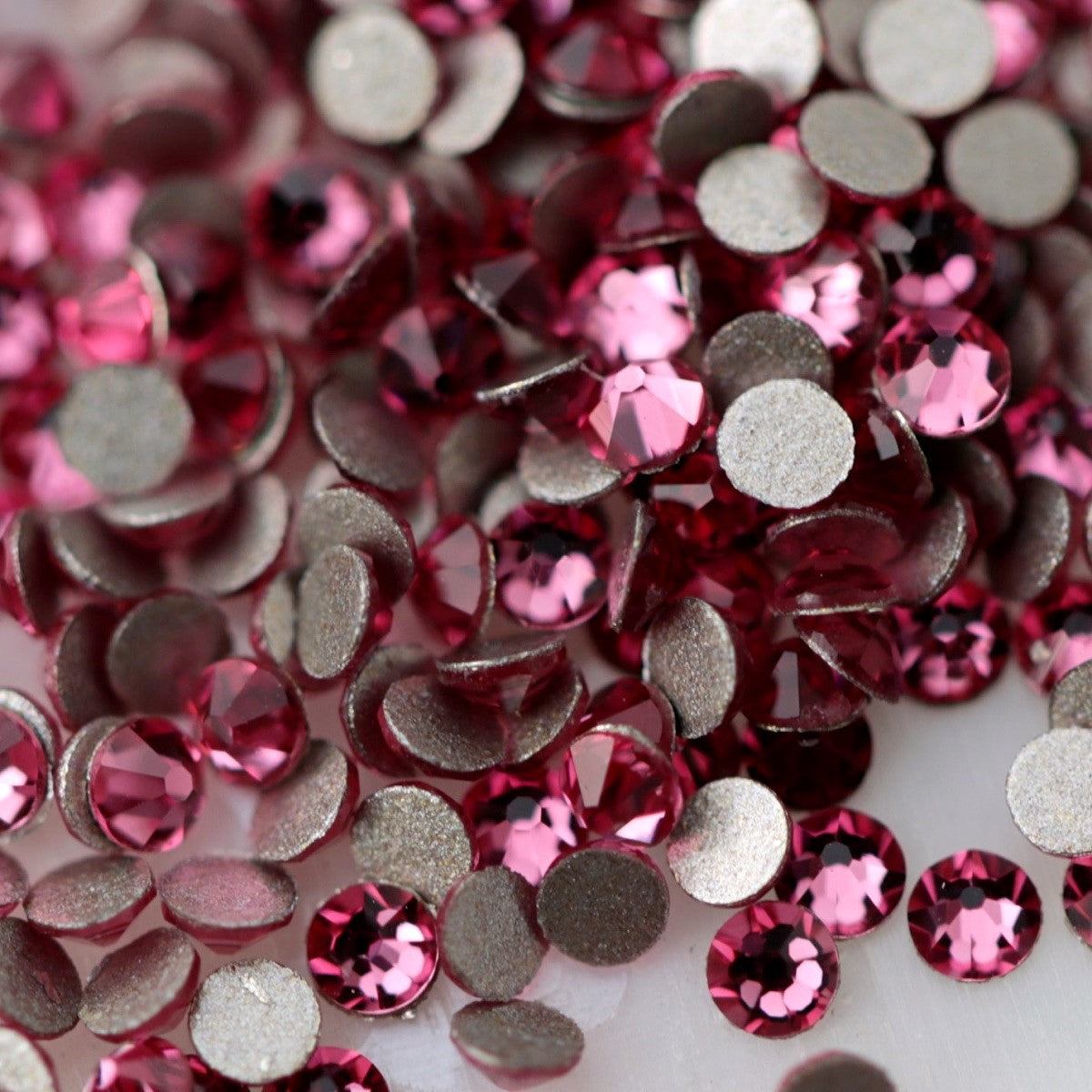 Close-up of round K9 flatback rhinestones in a medium Rose pink shade, showing defined faceting and bright pink, berry and subtle silvery reflections.