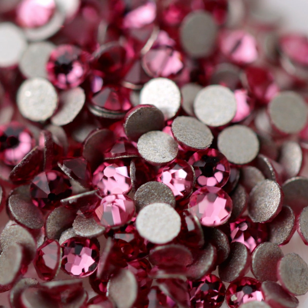 Rose pink K9 flatback rhinestones displayed from the front and back, highlighting their reflective faceted tops and flat backs for nail-art application.