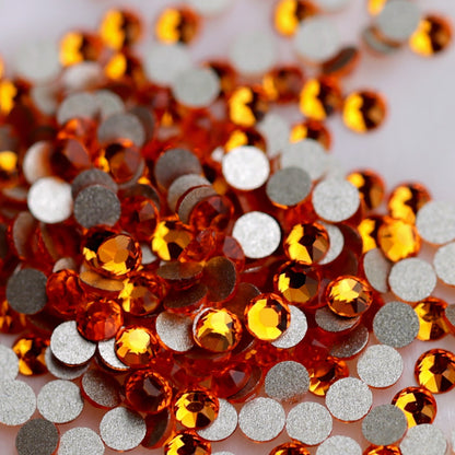 Tangerine K9 flatback rhinestones displayed from the front and back, highlighting their reflective orange faceted tops and flat backs for nail-art application.