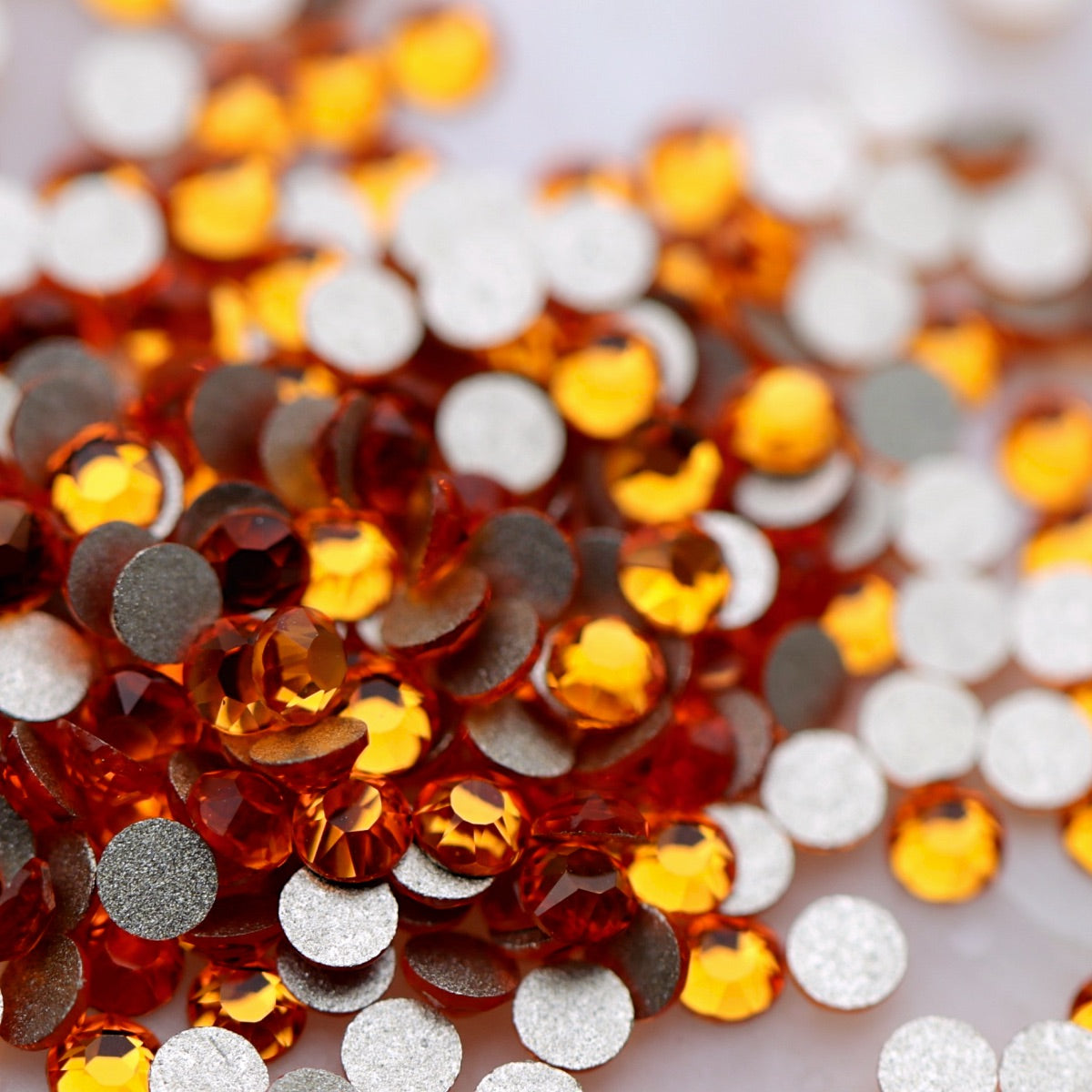 Close-up of round K9 flatback rhinestones in Tangerine, showing sharp faceting and transparent vivid-orange, mandarin, amber and golden reflections.