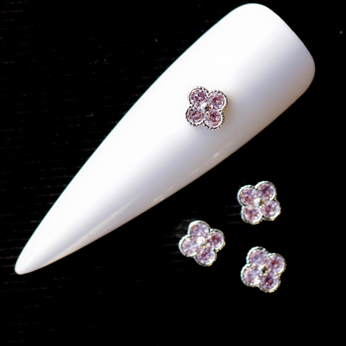 Flower-shaped nail charm decorated with four pink cubic zirconia stones arranged around a small central accent. The stones are set in a bright silver-tone base, creating an elegant floral nail jewellery decoration suitable for bridal manicures, romantic designs, wedding nails and delicate accent nail art.