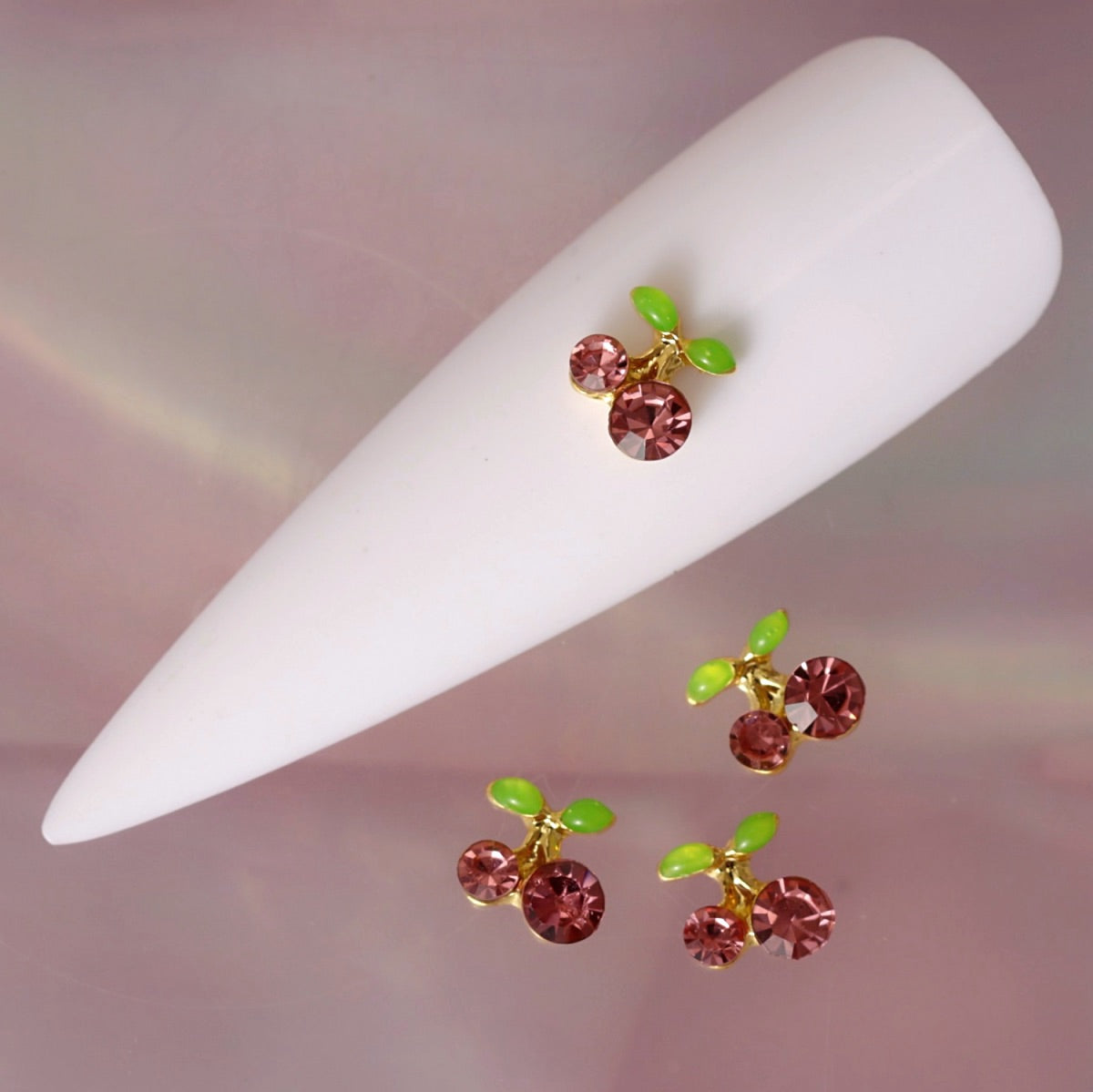 Cherry nail charm featuring two faceted pink rhinestone cherries, small green leaves and a polished gold-tone stem. This cute fruit-inspired decoration is ideal for summer manicures, kawaii nail art, romantic designs and playful accent nails.
