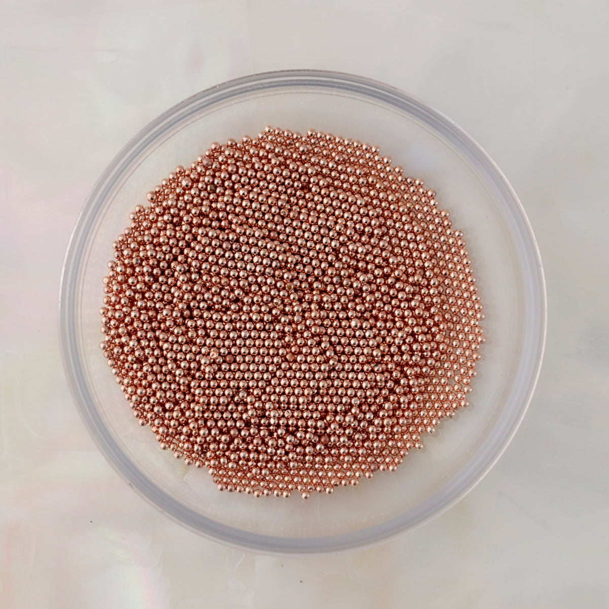 Close-up of small round rose gold metal caviar beads in several diameters for nail-art decoration.