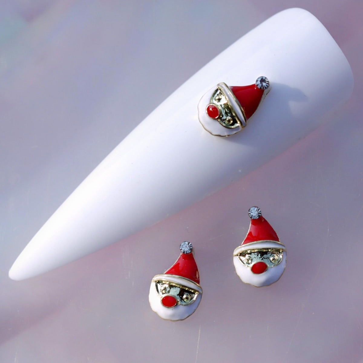 Santa Claus face nail charm featuring a red hat with white trim, a white beard, a bright red nose, gold-tone details and a clear rhinestone at the tip of the hat. This festive Christmas nail decoration is ideal for holiday manicures, winter nail art, Christmas parties and seasonal accent nails.