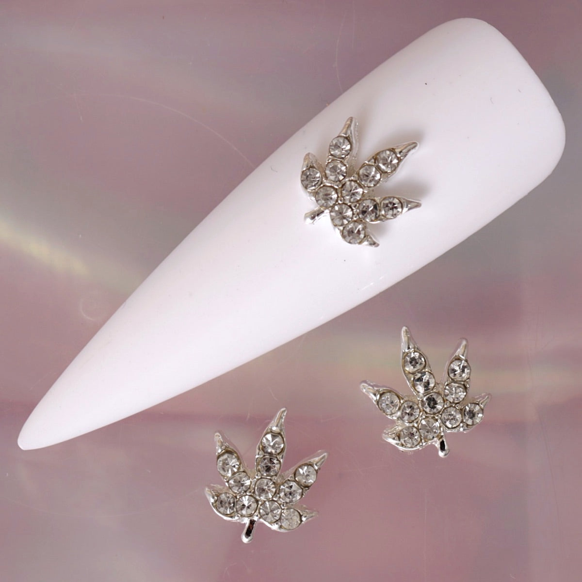 Silver cannabis leaf nail charm with polished metallic contours and multiple clear rhinestones arranged across the leaf sections. This bold decorative charm is ideal for statement manicures, festival nail art, alternative designs, party looks and glamorous crystal accent nails.