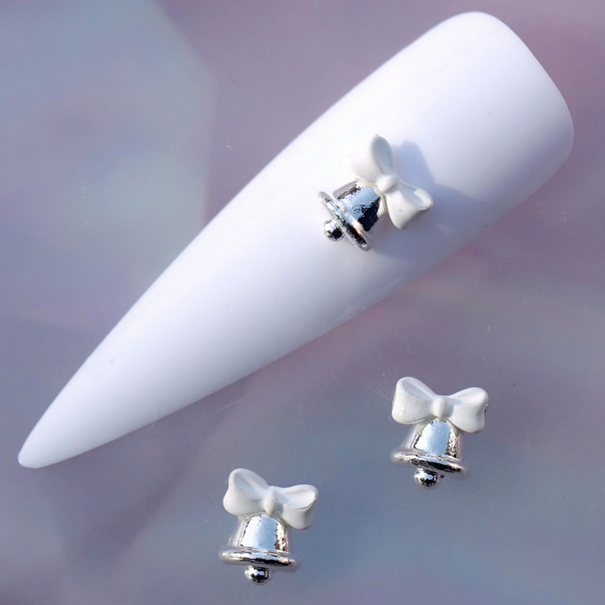 Silver-tone Christmas bell nail charm decorated with a soft white bow and a small rounded clapper. This elegant festive nail decoration is ideal for Christmas manicures, winter nail art, holiday parties, gift-inspired designs and seasonal accent nails.