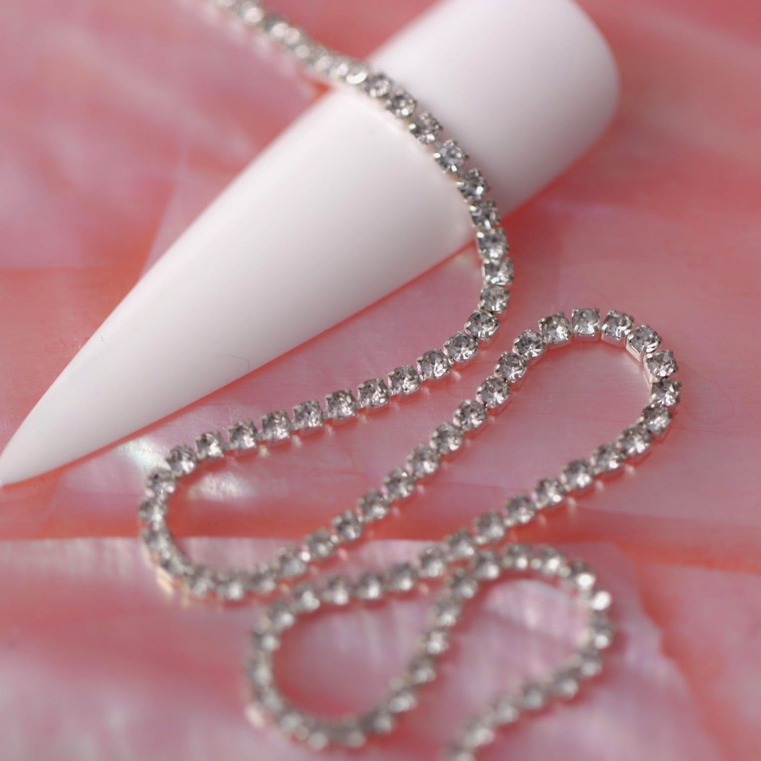 Silver 1.5 mm clear crystal rhinestone nail art chain laid across a white nail tip