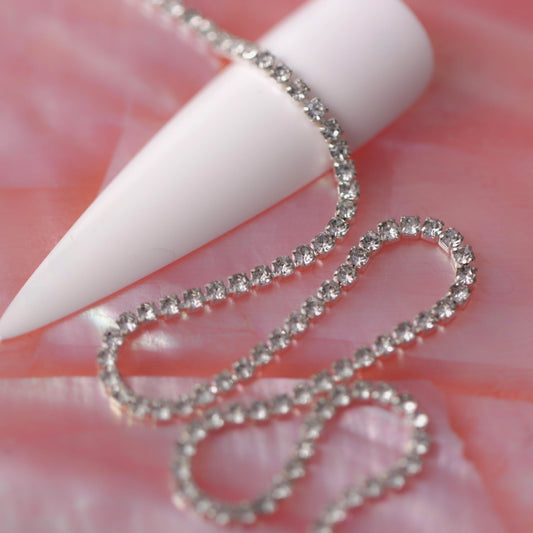 Silver 1.5 mm clear crystal rhinestone nail art chain laid across a white nail tip