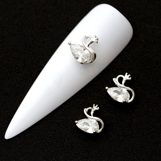Silver swan nail charms with raindrop‑shaped crystal CZ bodies and tiny crown stones on a white nail tip against a black background