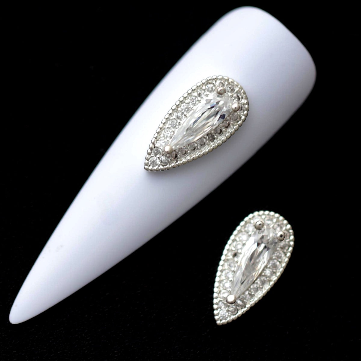 Silver teardrop halo nail charms with crystal CZ outline and large raindrop‑shaped centre stone on a white nail tip against a black background
